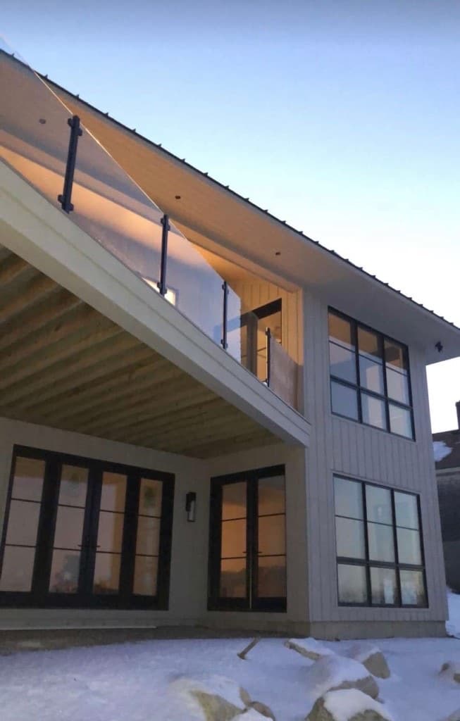 Two-story home with glass balcony railing and large glass doors